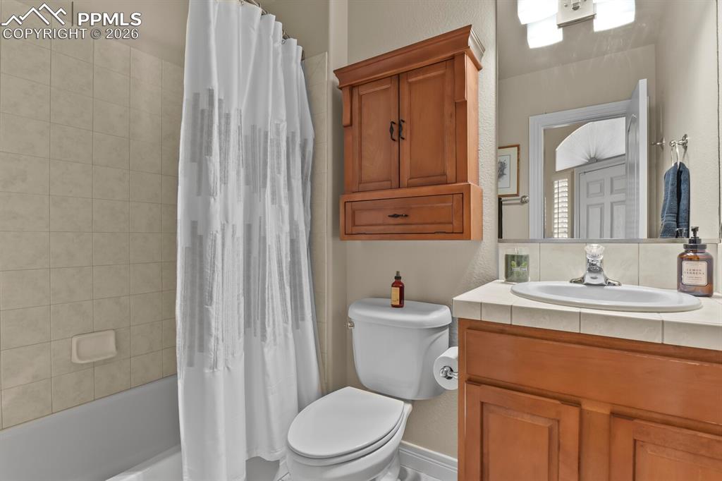 617 Concerto Drive Colorado Springs, CO 80906 - Photo 22 of 46 Main floor Bathroom featuring a built-in bathtub with tiled surround, a toilet, and a vanity with a tile countertop and wood cabinet