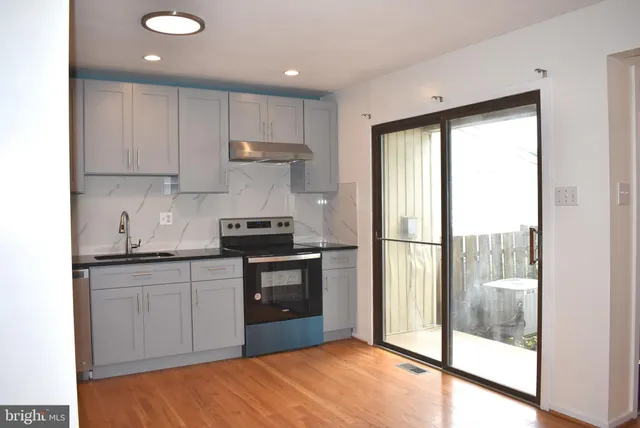 a kitchen with kitchen island granite countertop a refrigerator a sink a stove and white cabinets with wooden floor