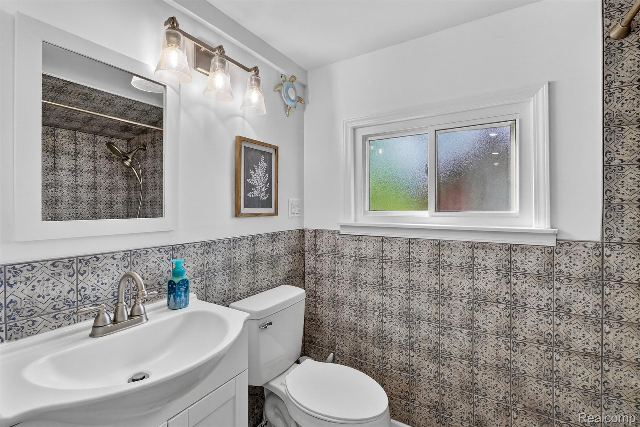 1717 Triangle Lake Road Howell, MI 48843 - Photo 50 of 58 Bathroom with vanity, toilet, white-framed mirror, and a window featuring decorative tile wainscoting and a matching shower surround