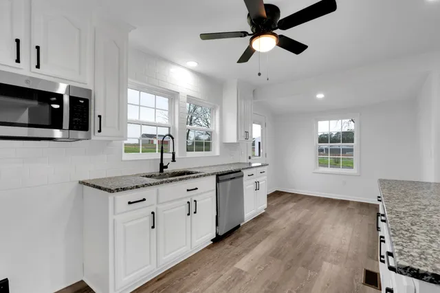a kitchen with granite countertop a sink cabinets stainless steel appliances and a large window