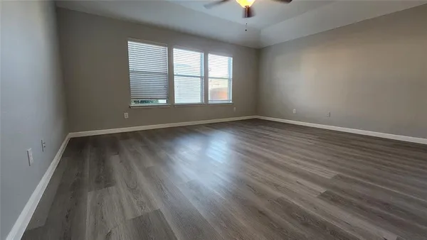 an empty room with wooden floor chandelier fan and windows