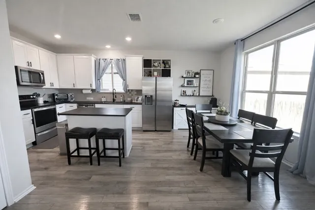 a kitchen with stainless steel appliances granite countertop a dining table chairs stove refrigerator and microwave