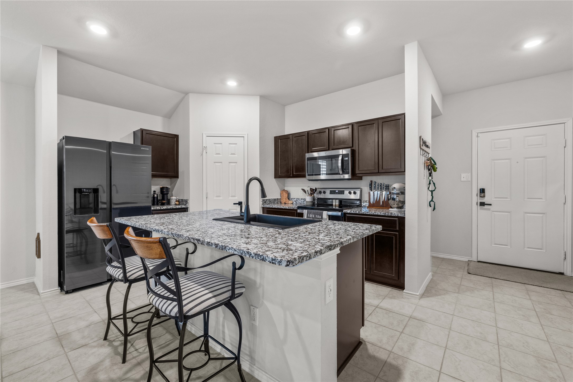 583 Taggart Trail Jarrell, TX 76537 - Photo 11 of 21 Kitchen with dark wood finish cabinets, stainless steel appliances, a breakfast bar, an island with sink, and light stone counters