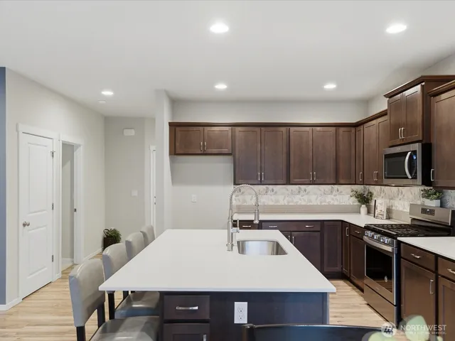 a open kitchen with kitchen island a stove a refrigerator a sink a dining table and chairs with wooden floor