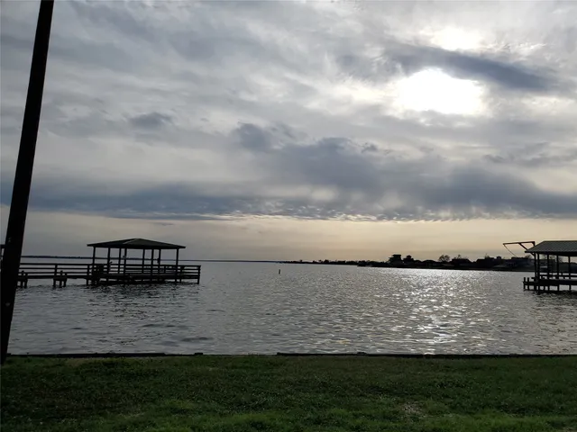 a view of a lake with lawn chairs and large trees