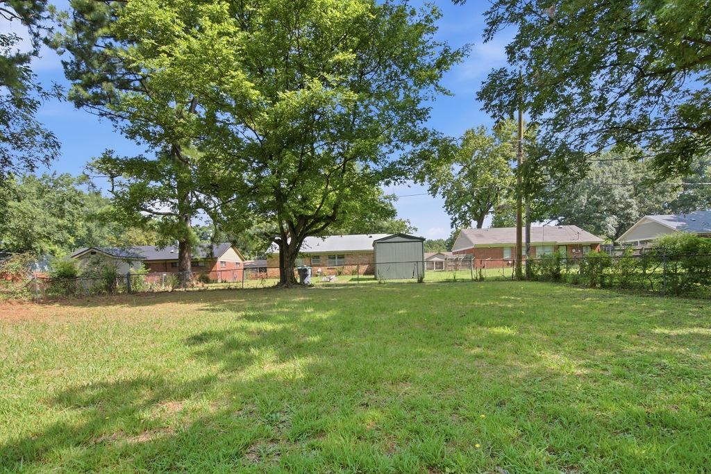 1304 Winfield Road Memphis, TN 38116 - Photo 19 of 19 Expansive green space with mature trees, offering a metal storage shed and partial chain-link fencing
