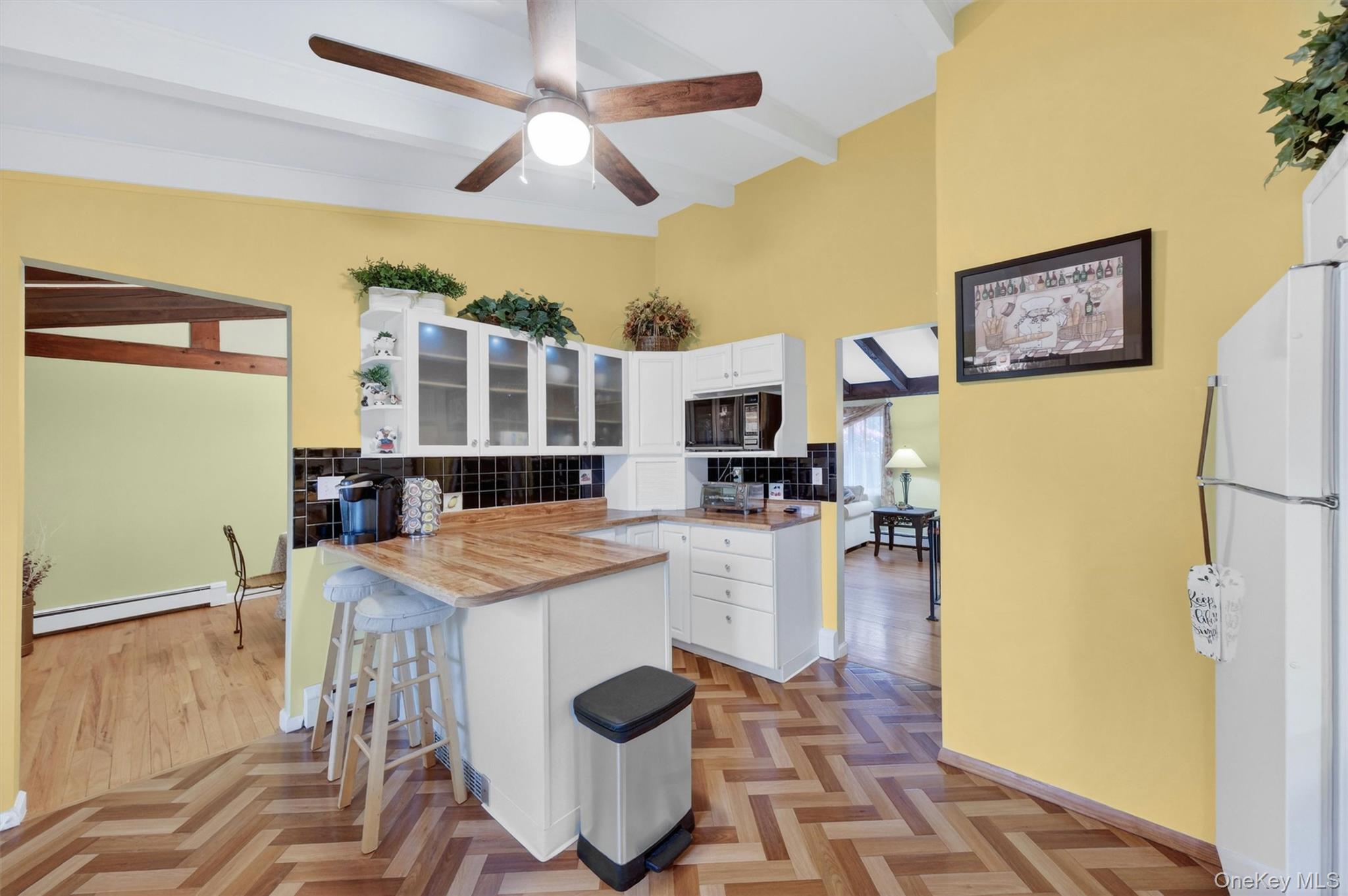 1 Rockledge Road Poughkeepsie, NY 12601 - Photo 11 of 36 Kitchen featuring vaulted ceilings with exposed beams, wood-finish flooring in a herringbone pattern, white cabinetry, breakfast bar, tile backsplash, cabinet lighting and light wood-finish countertops