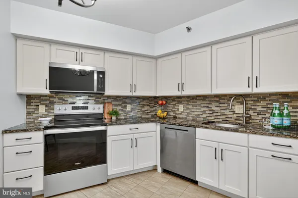 a kitchen with stainless steel appliances granite countertop a refrigerator a stove a sink dishwasher and white cabinets with wooden floor