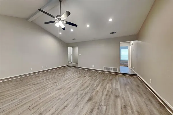 an empty room with wooden floor chandelier fan and windows