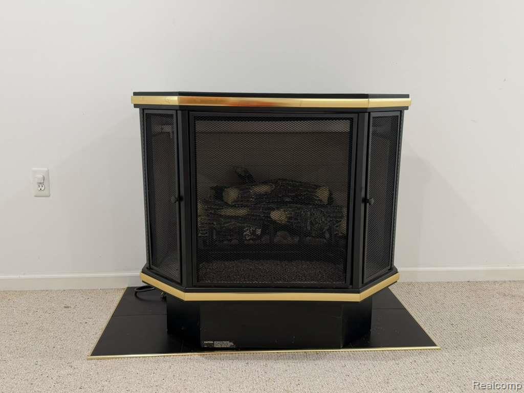 1154 Bluebird Drive Rochester, MI 48307 - Photo 31 of 34 Hexagonal freestanding fireplace with a black finish and gold-tone trim, featuring mesh screen doors, an artificial log set, and a black hearth pad