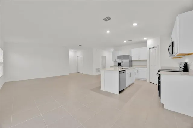 a large white kitchen with kitchen island a sink a center island stainless steel appliances and a refrigerator