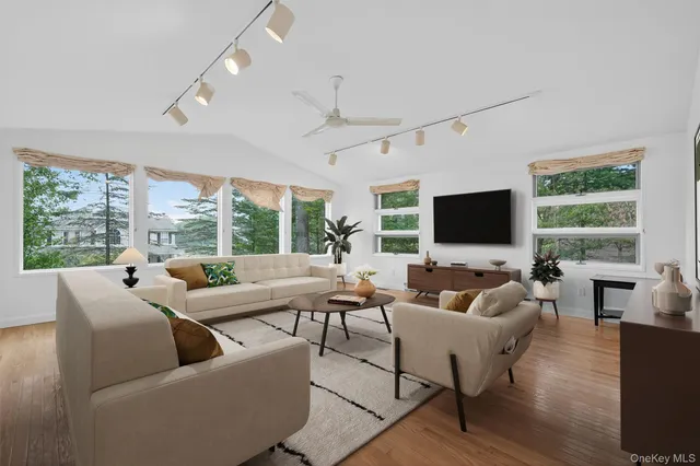 a living room with furniture floor to ceiling window hardwood floor and a flat screen tv