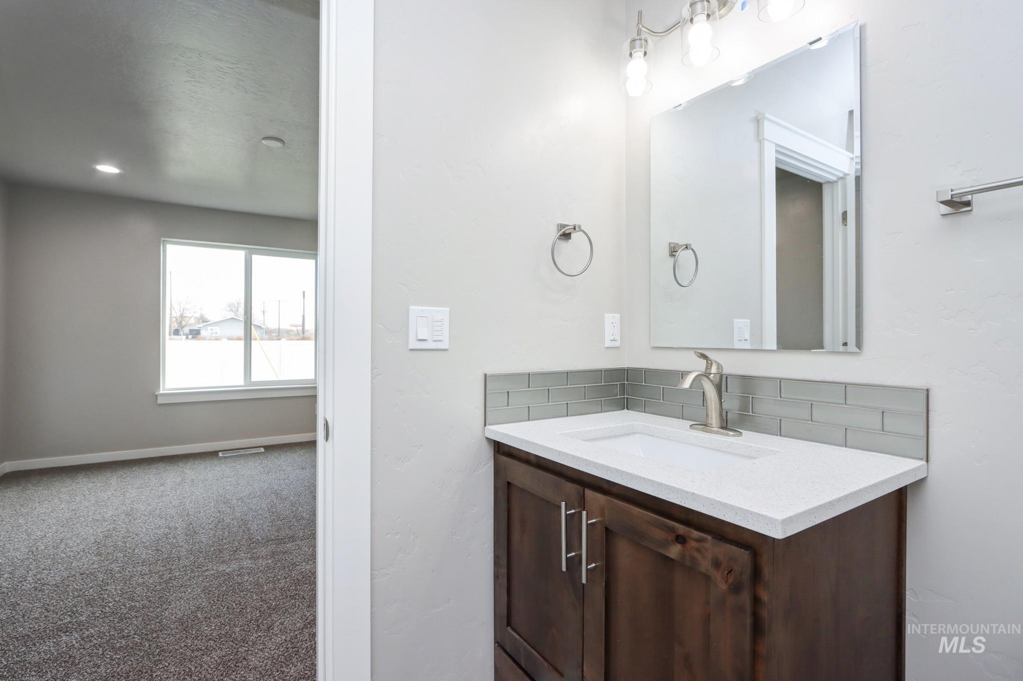824 North 5th Street Nyssa, OR 97913 - Photo 15 of 23 Bathroom featuring vanity, backsplash, carpet, and a textured wall