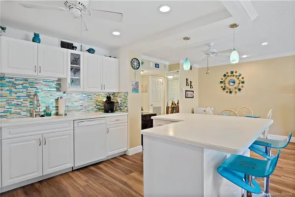 a open kitchen with kitchen island a stove a sink a refrigerator white cabinets with wooden floor