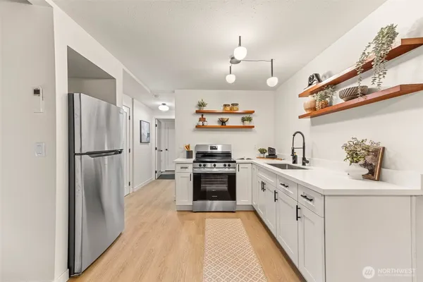 a kitchen with stainless steel appliances granite countertop a refrigerator a sink dishwasher a stove and white cabinets with wooden floor