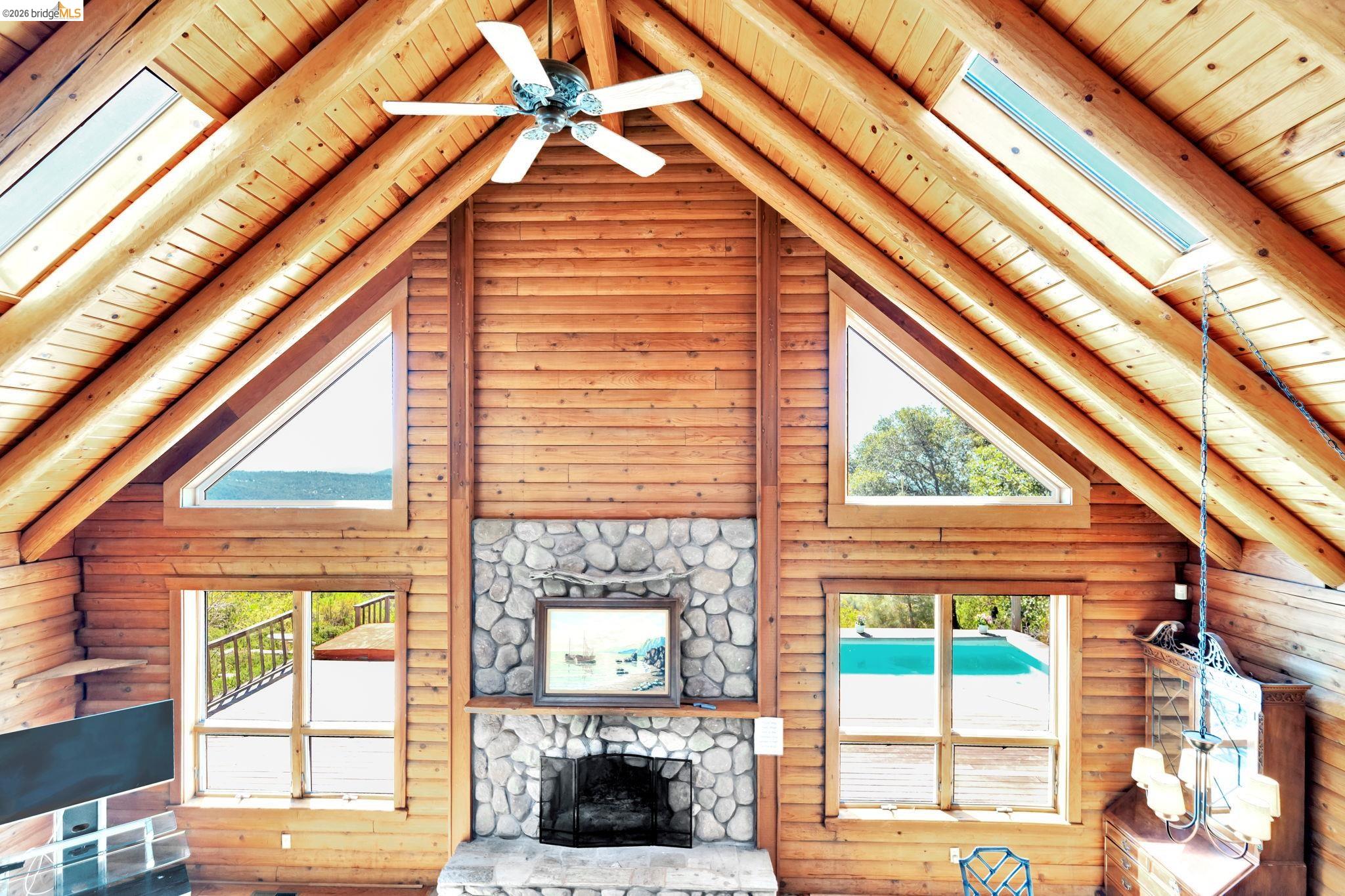 14799 Big Hill Road Sonora, CA 95370 - Photo 26 of 60 Living room with a high wood beamed ceiling, a fireplace, rustic walls, and a ceiling fan