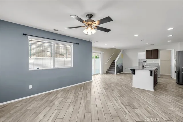 a view of a livingroom with kitchen appliances and a ceiling fan