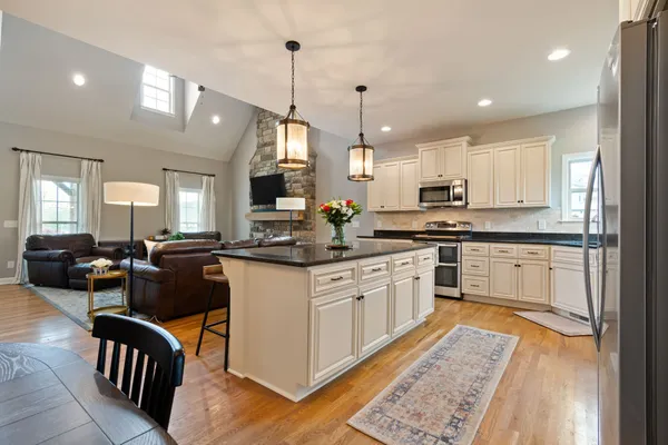 a kitchen with stainless steel appliances granite countertop a stove a sink dishwasher a refrigerator and white cabinets with wooden floor