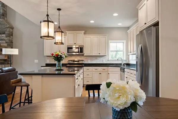 a kitchen with stainless steel appliances granite countertop a stove a refrigerator a sink a dining table and chairs with wooden floor