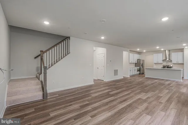 a view of empty room with wooden floor and kitchen