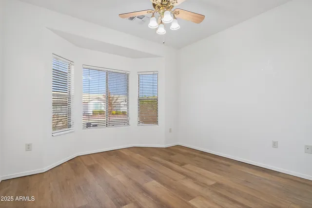 an empty room with wooden floor chandelier fan and windows