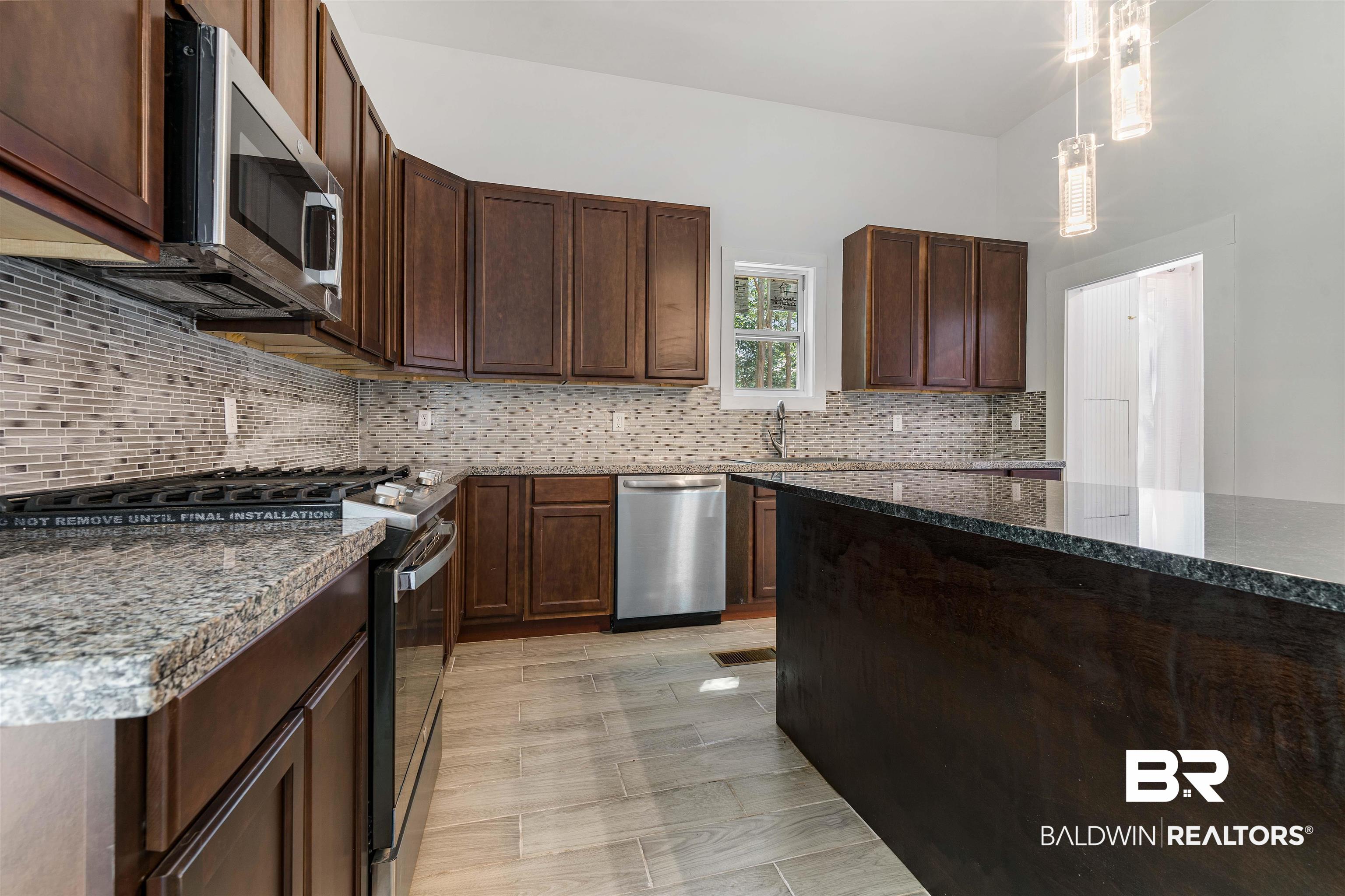 407 East 2nd Street Bay Minette, AL 36507 - Photo 10 of 40 Kitchen with appliances with stainless steel finishes, decorative light fixtures, dark stone countertops, tasteful backsplash, and dark brown cabinets