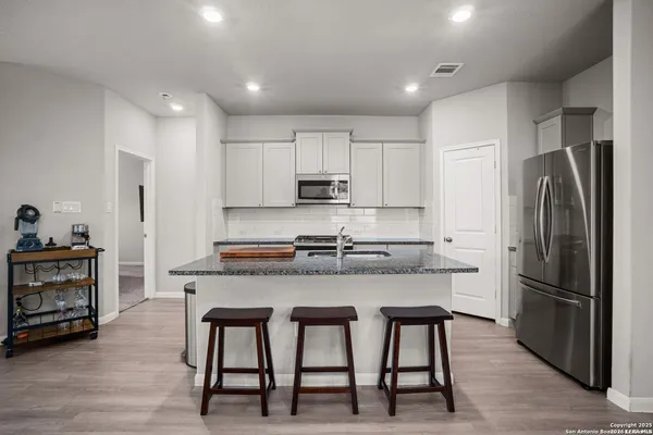 a kitchen with stainless steel appliances granite countertop a stove a refrigerator a sink a stove and white cabinets with wooden floor