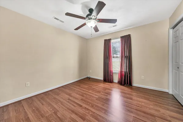 an empty room with wooden floor chandelier fan and windows
