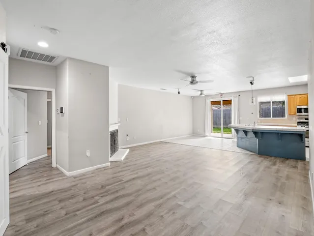 a view of an empty room with wooden floor and a kitchen