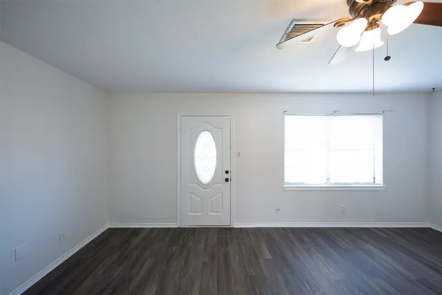 an empty room with wooden floor chandelier fan and windows