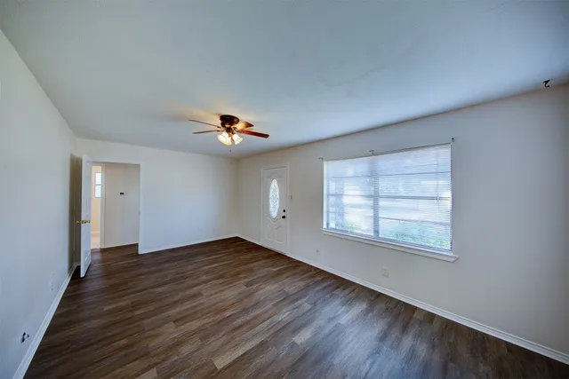 an empty room with wooden floor chandelier fan and windows