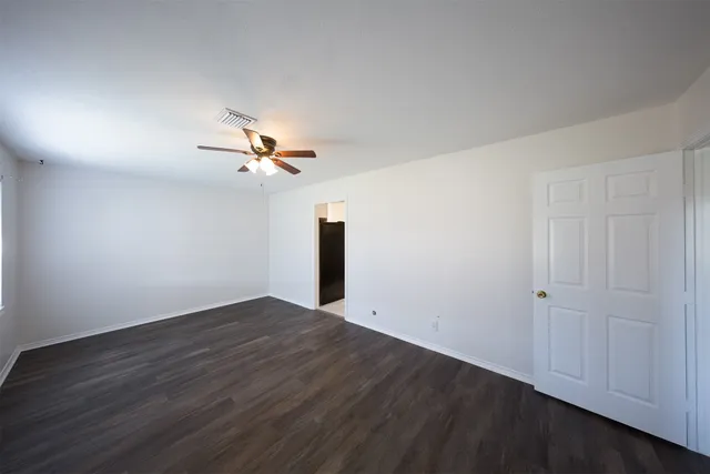 an empty room with wooden floor ceiling fan and windows