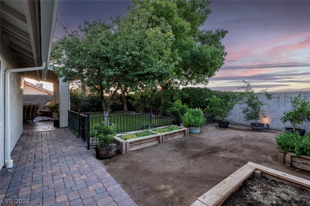 818 Manor Shores Road Henderson, NV 89002 - Photo 32 of 35 A private backyard oasis features a paved patio leading to raised garden beds and lush greenery.