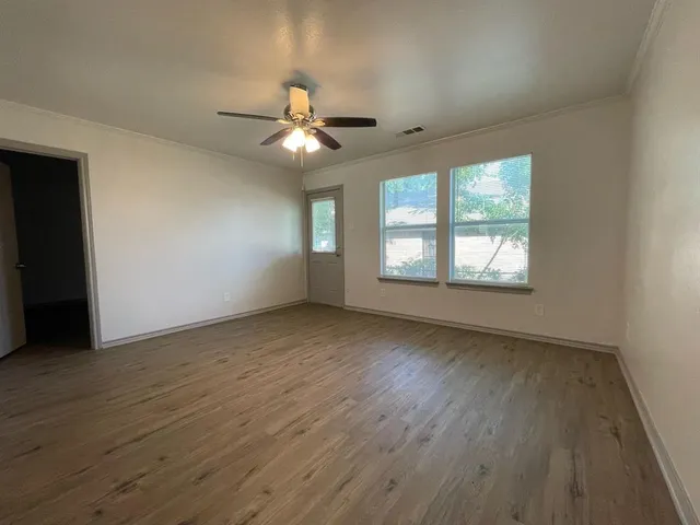 an empty room with wooden floor fan and windows