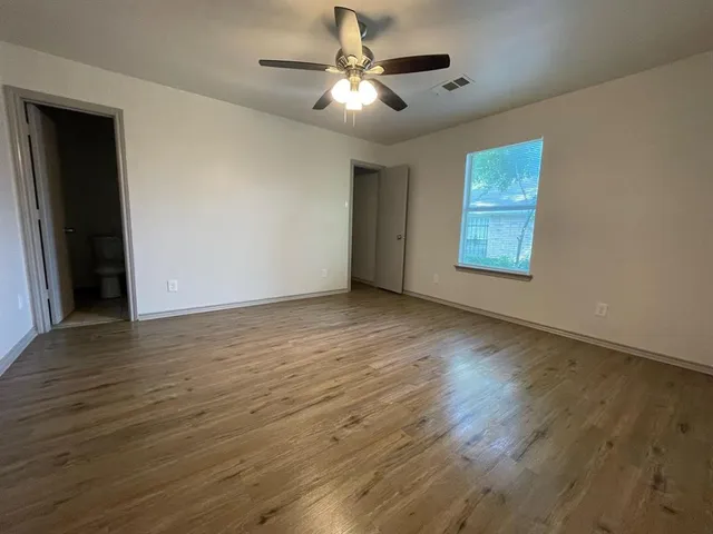 a view of an empty room with wooden floor and a ceiling fan