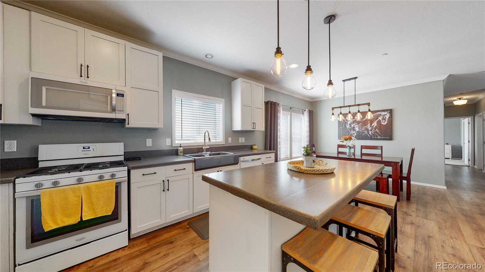 4038 Meadowlark Road Fort Lupton, CO 80621 - Photo 6 of 40 a kitchen with stainless steel appliances granite countertop a stove a sink dishwasher a microwave oven a dining table and chairs with wooden floor