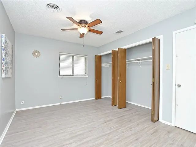 a view of an empty room with wooden floor and a ceiling fan