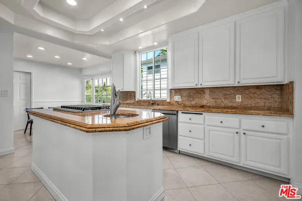 a kitchen with stainless steel appliances granite countertop a sink a window and white cabinets