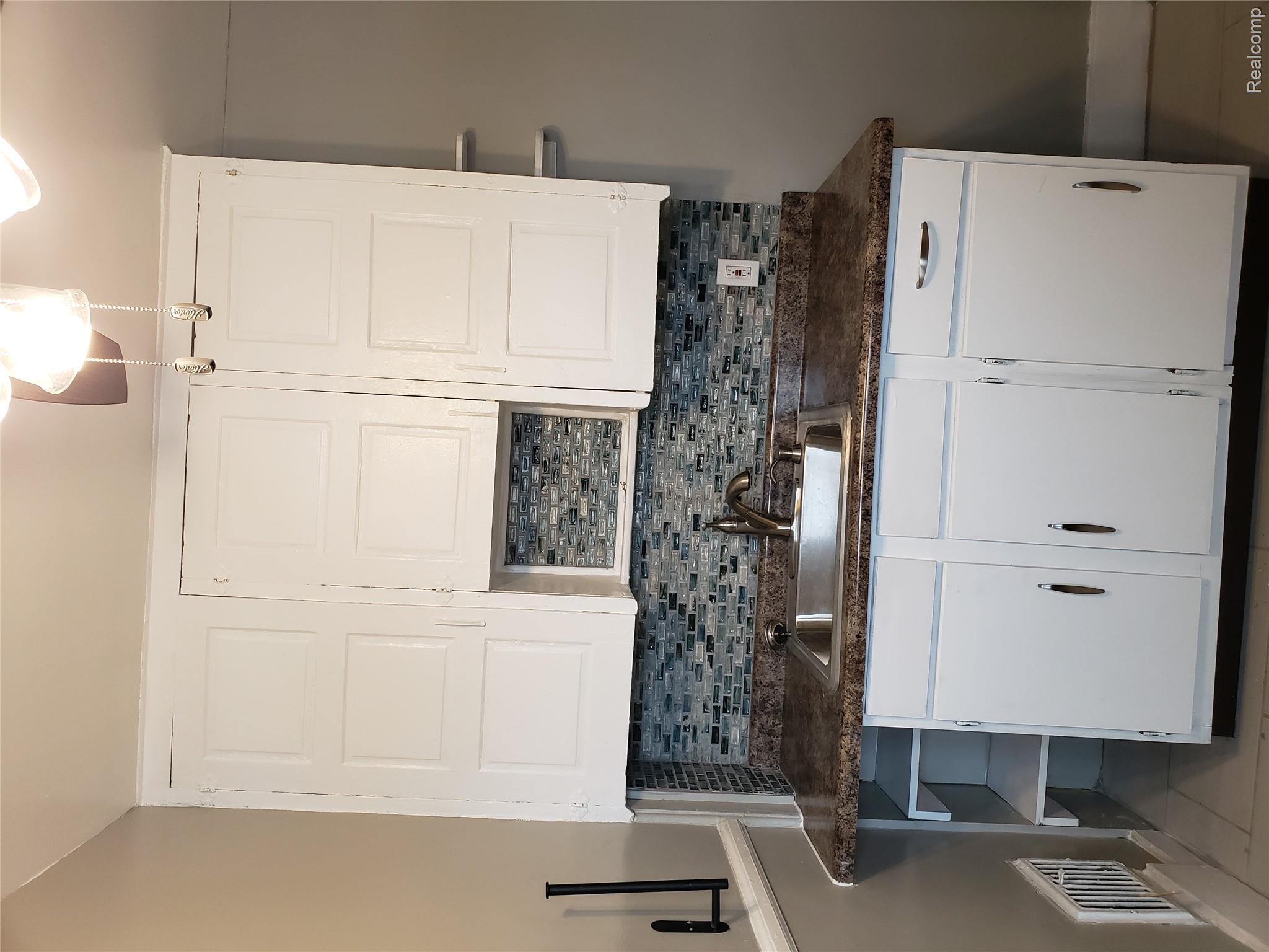 15381 Prairie Street Detroit, MI 48238 - Photo 10 of 22 White cabinetry with dark hardware, a stainless steel sink, and a multi-tone tile backsplash