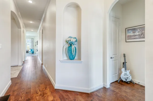 an empty room with wooden floor and way to kitchen
