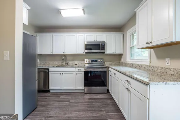 a kitchen with stainless steel appliances granite countertop a stove top oven a sink dishwasher and a refrigerator with wooden cabinets