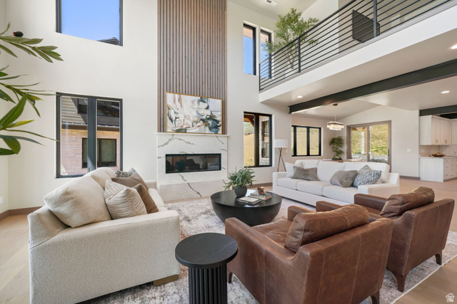 10646 North Reflection Ridge Hideout, UT 84036 - Photo 7 of 43 Two-story great room with a linear fireplace set into a large-format veined stone surround, vertical wood accent paneling, and an upper-level balcony featuring horizontal metal railings