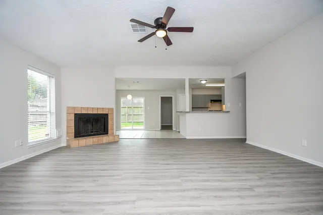 a view of a livingroom with a fireplace a ceiling fan and windows