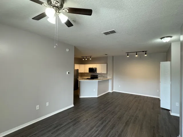 an empty room with wooden floor a ceiling fan and kitchen view