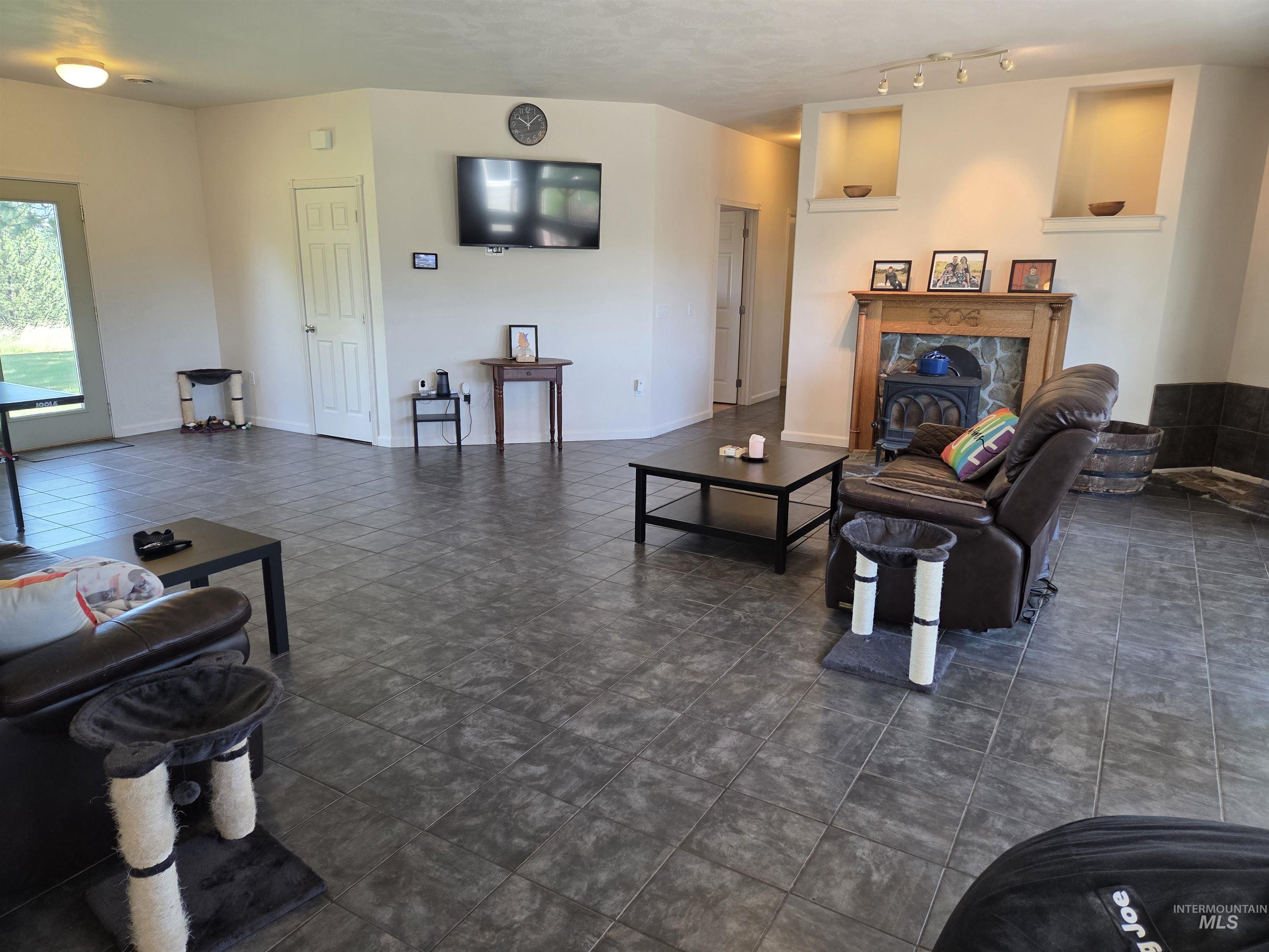 1085 Wallen Road Moscow, ID 83843 - Photo 14 of 50 Spacious room featuring dark-toned tile flooring, a prominent fireplace with a wood mantel and stone surround, built-in wall niches with integrated lighting, and a white paneled door