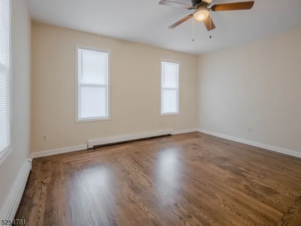 an empty room with wooden floor chandelier fan and windows