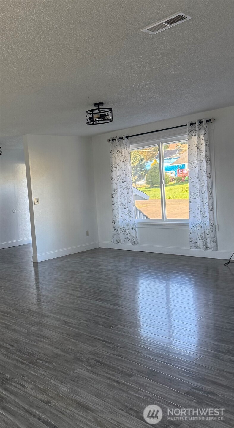 1017 Ballentine Street Raymond, WA 98577 - Photo 6 of 33 an empty room with wooden floor and windows
