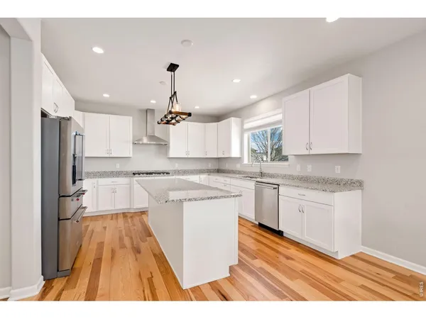 a kitchen with stainless steel appliances granite countertop a sink dishwasher a refrigerator and white cabinets with wooden floor