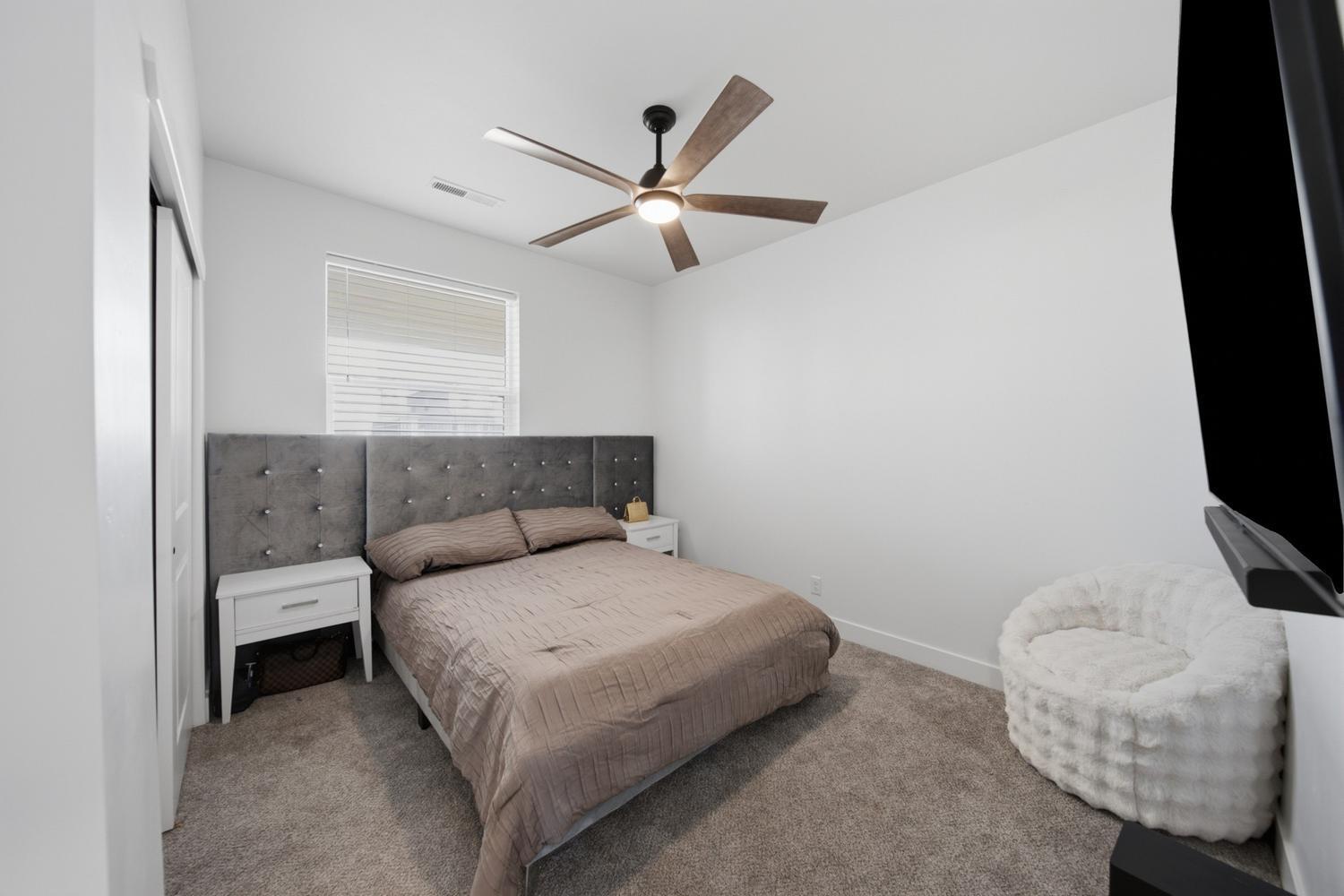 6144 Red Sand Lane St. George, UT 84790 - Photo 11 of 19 Comfortably sized and move-in ready, this secondary bedroom offers a tufted charcoal headboard, plush carpeting, and a ceiling fan for year-round comfort. Twin nightstands flank the bed, while a large window brings in soft natural daylight — a versatile retreat for guests or a growing family.