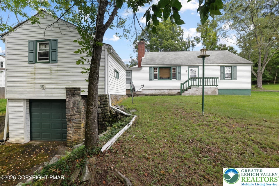 Mature trees frame a classic white exterior complete with an integrated lower-level garage.